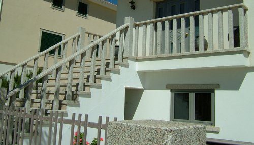 Balaústres em granito de escadas e varanda de uma habitação unifamiliar. Também se pode ver as janelas e os pilares do muro, ambos em granito.